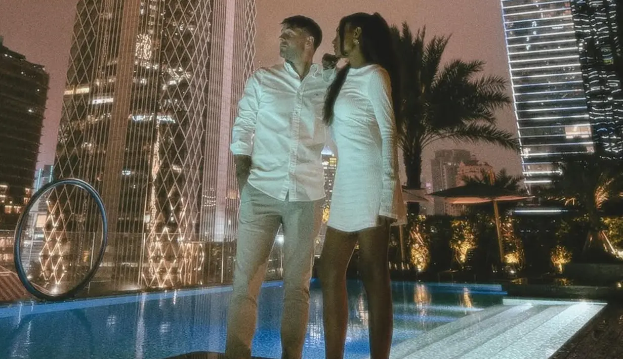 Novia dan kekasih berpose mesra di pinggir kolam renang yang berada di rooftop gedung bertingkat, dikelilingi pencahayaan malam kota yang gemerlap. Suasana yang romantis dan mewah membuat keduanya merasa semakin nyaman menghabiskan waktu bersama. (Liputan6.com/IG/@noviabachmid)