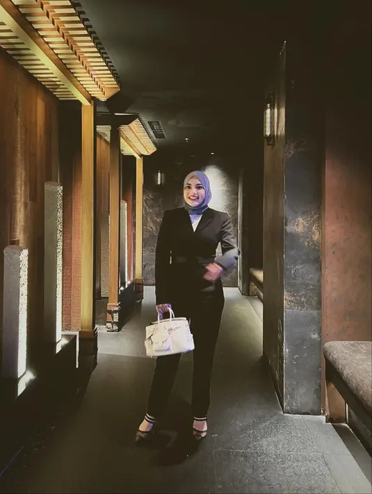 Padu padan blazer hitam untuk kamu yang berhijab ala Aurelie Hermansyah. Di sini, ia tampak mengenakan setelan blazer dengan dua kantung dan celana panjang hitam yang serasi. Ia padukan dengan innerwear berwarna putih, hijab ungu, dan heels yang juga berwarna hitam. Foto: Instagram.