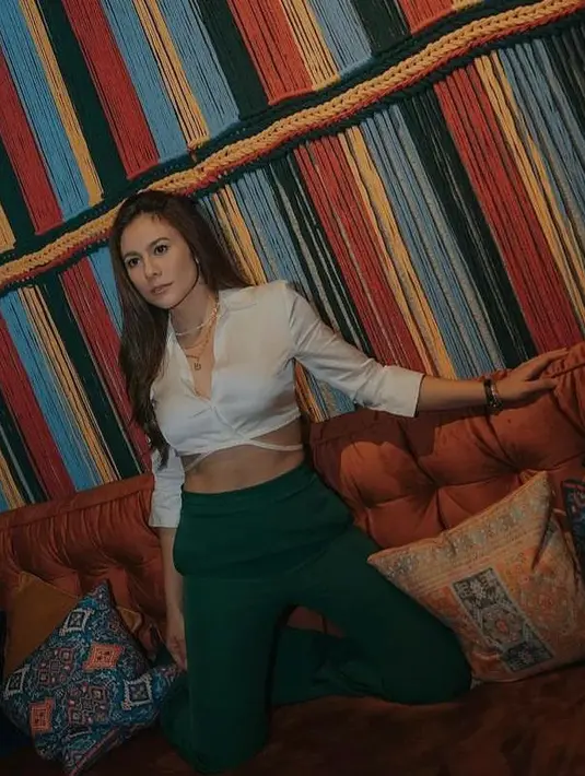 <p>Gaya edgy Wulan memadukan wrap cross tie blouse top warna putih dan high waist hijau emerald. (Instagram/wulanguritno).</p>