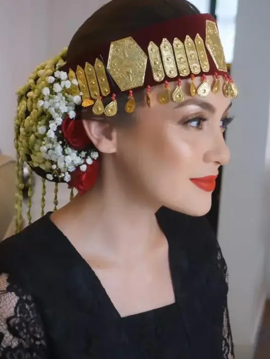 Untuk rambutnya, hair stylist  @meli_makeuphairdowedding menata rambut Rianti dengan sanggul klasik. Dipermanis dengan hiasan kepala Batak bernama sortali dan beberapa bunga. [@riantic/@__rose_makeupartist/@meli_makeuphairdowedding]