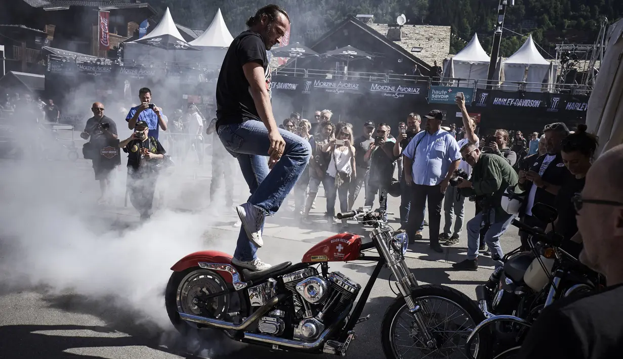 Seorang pria melakukan aksi berdiri diatas motor saat acara 6th Morzine-Avoriaz Harley Days 2017, Morzine (15/7). Sekitar 10.000 sepeda motor dan 30.000 bikers dari seluruh Eropa berkumpul untuk mengikuti acara ini. (AFP Photo/Jean-Philippe Ksaizek)