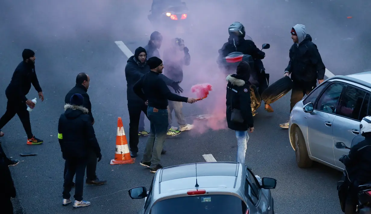 Seorang sopir taksi memegang suar api sambil memblokir jalan saat unjuk rasa menentang layanan transportasi VTC seperti Uber, di jalan lingkar di porte Maillot di Paris, Perancis, Selasa (26/1). (AFP PHOTO/Thomas SAMSON)