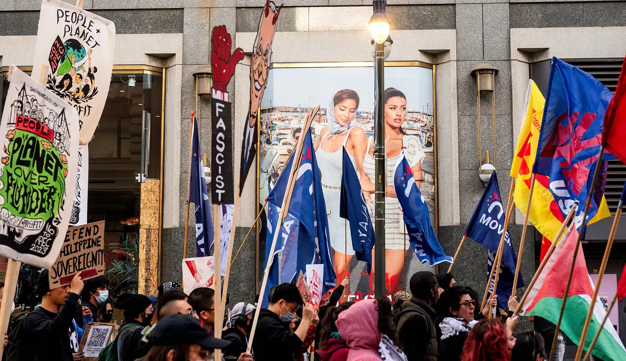 Para demonstran melewati sebuah iklan saat berunjuk rasa menentang KTT APEC (Kerja Sama Ekonomi Asia Pasifik), Minggu, 12 November 2023, di San Francisco. (AP Photo/Noah Berger)