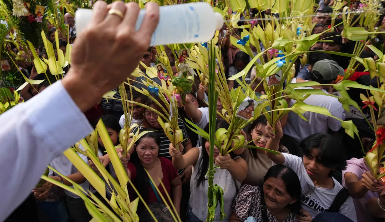 Daun palem digunakan sebagai simbol kemenangan dan damai. Tampak dalam foto, seorang pekerja gereja memercikkan air suci ke daun palem para umat selama upacara pemberkatan di luar Katedral Antipolo, kota Antipolo, provinsi Rizal, Filipina, saat memperingati Minggu Palma, 29 Maret 2026. (AP Photo/Aaron Favila)