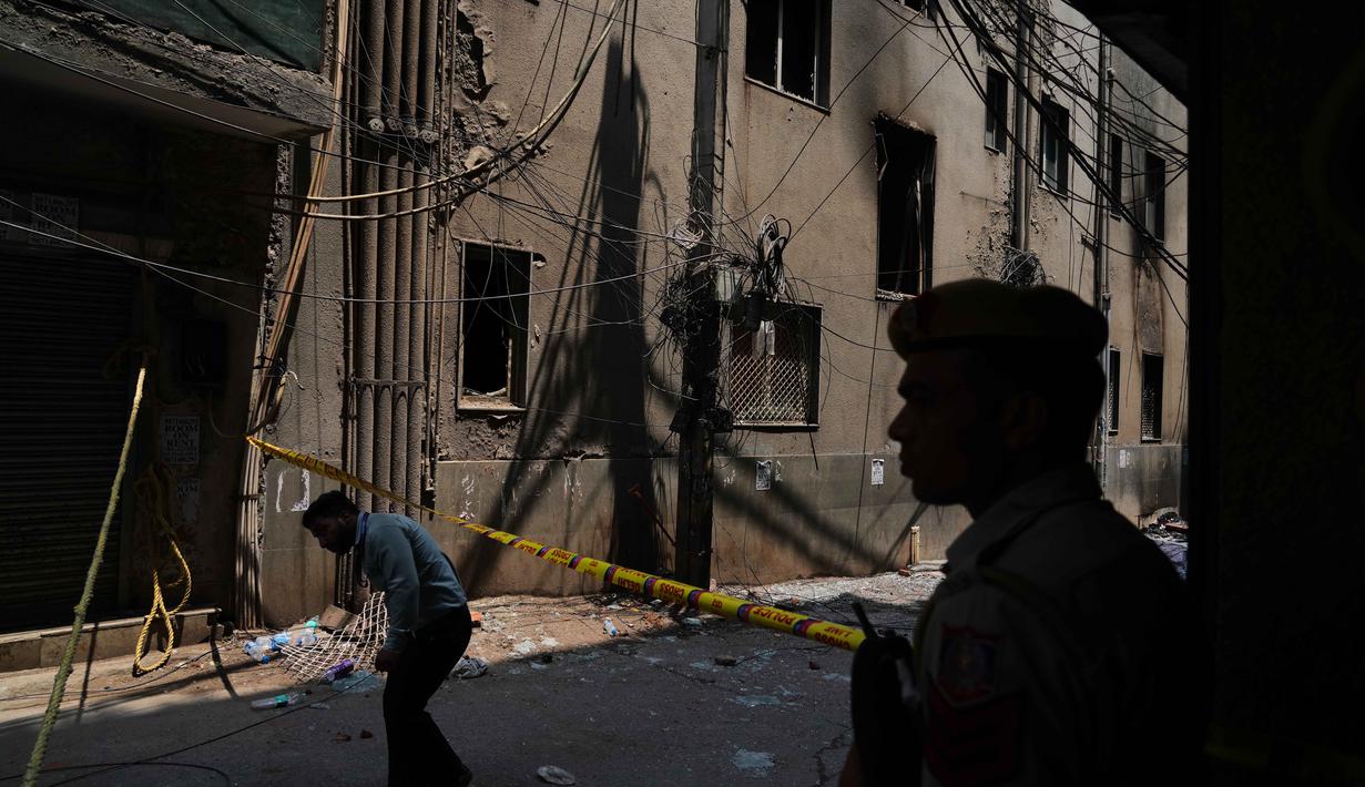 Seorang polisi berjaga saat warga setempat berjalan melewati gedung restoran dan hotel yang terbakar di New Delhi, India, Rabu 3 Juni 2026. (AP Photo/Manish Swarup)