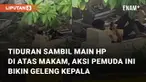 Aksi seorang pemuda tiduran sambil bermain hp di atas makam mengundang perhatian