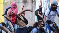 Demonstran melemparkan batu ke arah polisi anti huru hara selama protes terhadap kebijakan ekonomi pemerintah di Santiago (6/11/2019). Para pemrotes meminta para demonstran untuk memperluas aksi unjuk rasa. (AFP Photo/Martin Bernetti)