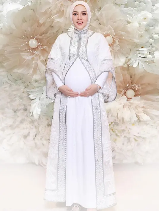 Saat syukuran kehamilan 7 bulanan, Syahrini tampil serba putih mengenakan outer embroidery silver dengan inner dress putih senada dengan kerudungnya. Ia juga tampil dengan makeup natural clean.  [@princessyahrini]