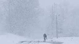 Seorang pria berjalan di bawah salju lebat saat terjadi badai salju di Manville, New Jersey (21/3). Salju tebal yang menutup jalanan ini berpotensi membahayakan warganya. (AP/Julio Cortez)
