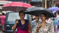 Dua orang wanita berjalan sambil menggunakan payung saat hujan mengguyur kota Gauhati, India, Selasa (30/5). Beberapa negara bagian di India timur laut mengalami hujan deras sebagai efek topan Mora yang melanda selatan Bangladesh. (AP Photo/ Anupam Nath)
