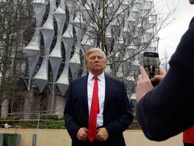 Seorang pria mengambil gambar lilin Madame Tussauds Presiden AS Donald Trump yang dipajang di luar Kedutaan Besar AS yang baru di Nine Elms, London (12/1). Donald Trump telah membatalkan rencana kunjungannya ke London. (AP Photo / Alastair Grant)