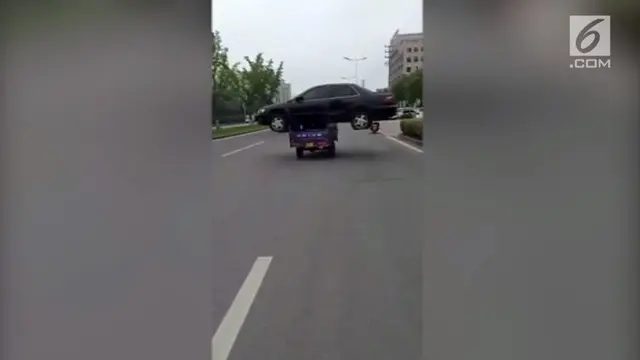 Sebuah kendaraan roda tiga mengangkut mobil sedan dan melaju di jalan raya Kota Huzhou. Polisi akhirnya memberikan denda kepada si pengemudi.