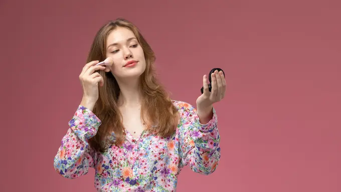 Seorang perempuan sedang mengaplikasikan makeup di bagian pipinya (Foto Dok: Freepik/KamranAydinov)