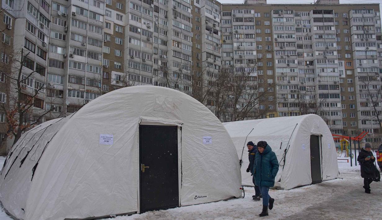 Tenda-tenda darurat pun didirikan di sejumlah titik sebagai langkah sementara untuk membantu warga bertahan dari dinginnya musim dingin. Tampak dalam foto, warga melewati salah satu tenda darurat tempat orang-orang dapat menghangatkan diri setelah serangan udara rutin Rusia terhadap fasilitas energi negara itu di tengah musim dingin, Kyiv, Ukraina, Selasa 13 Januari 2026. (AP Photo/Efrem Lukatsky)