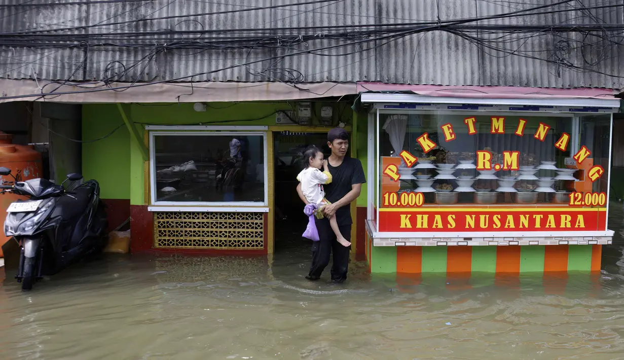 Dengan ketinggian air bervariasi, banjir rob di kawasan Muara Baru Jakarta juga merendam akses jalan utama. Tampak dalam foto, seorang pria menggendong anak membeli makanan siap saji di sebuah rumah makan saat jalanan terendam banjir akibat pasang tinggi di Muara Baru, Jakarta, pada Sabtu 6 Desember 2025. (ADITYA IRAWAN/AFP)