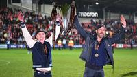 Aktor Hollywood, Ryan Reynolds (kanan) dan pemilik klub Wrexham, Rob McElhenney merayakan kesuksesan dengan mengangkat trofi setelah klub mereka berhasil promosi ke Liga Dua Inggris. Wrexham menang atas Boreham Wood dengan skor 3-1 pada laga English National League di Racecourse Ground Stadium, Wrexham, Wales, Sabtu (22/04/2023). (AFP/Oli Scarff)