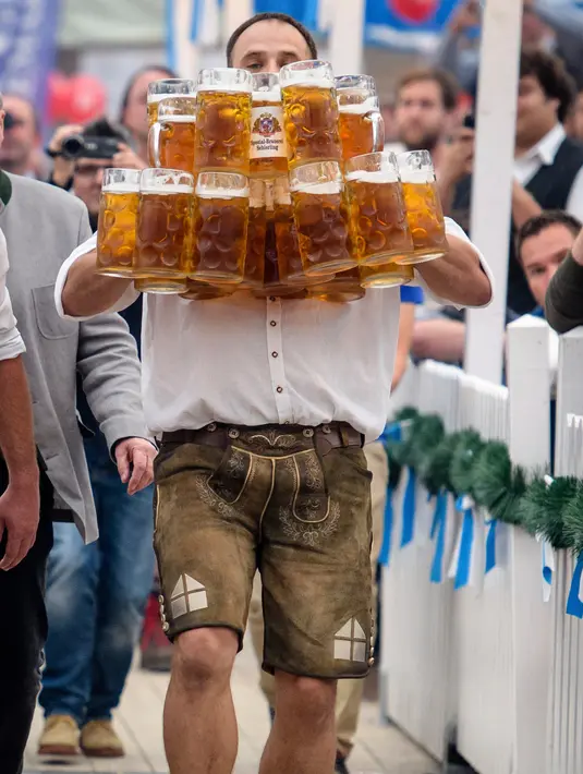 Oliver Struempfel berjalan membawa sejumlah gelas bir besar dalam festival tradisional Gillamoos di Abensberg, Jerman, Minggu (3/9). Struempfel berhasil memecahkan rekor membawa 29 gelas bir dengan berjalan sejauh 40 meter. (Matthias Balk/dpa via AP)