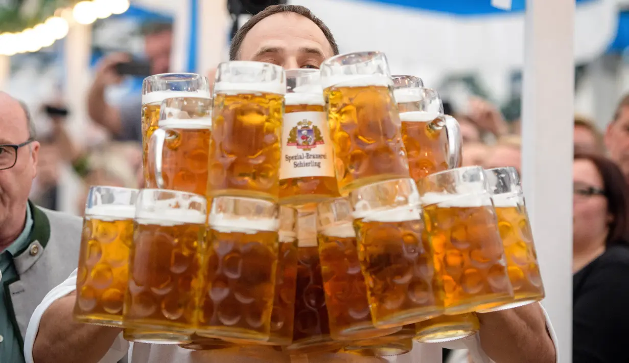 Oliver Struempfel membawa gelas bir sebanyak-banyaknya sambil berjalan untuk memecahkan rekor saat bersaing pada festival tradisional Gillamoos di Abensberg, Jerman, Minggu (3/9). Struempfel berhasil menyusun 29 gelas bir besar. (Matthias Balk/dpa via AP)