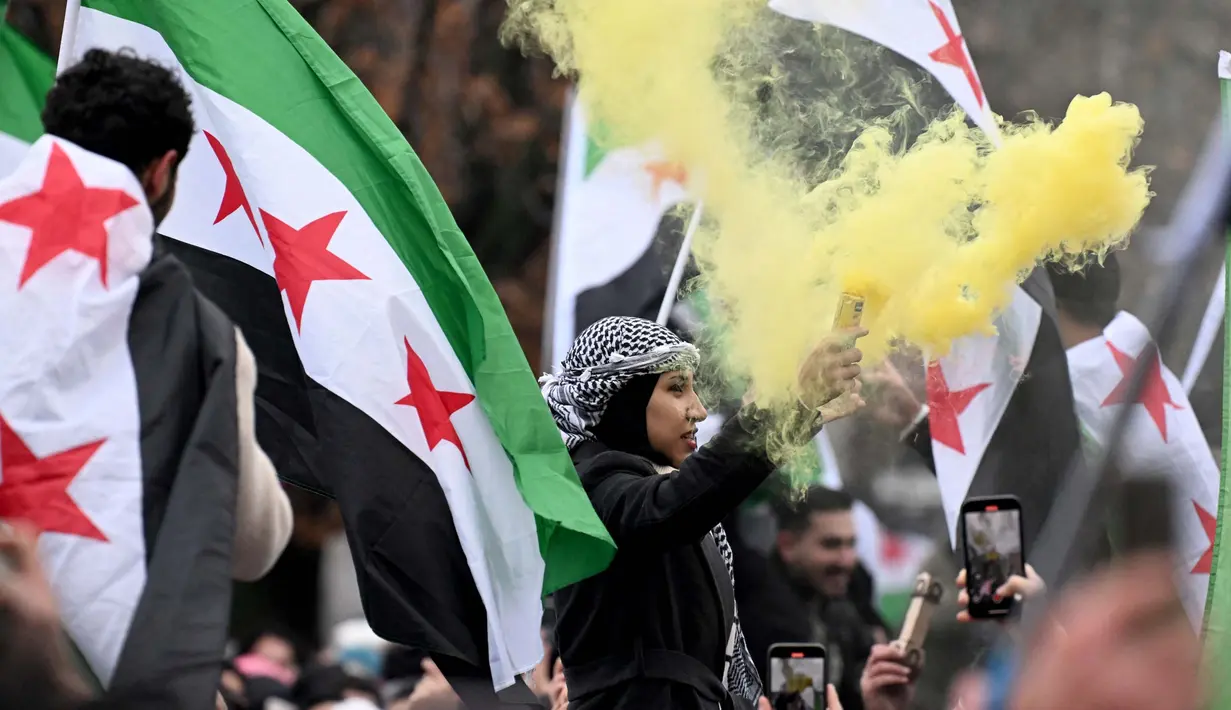Pemberontak yang dipimpin oleh kelompok Islamis menggulingkan penguasa lama Suriah, Bashar al-Assad. Tampak dalam foto, anggota komunitas Suriah melambaikan bendera Suriah dan menyalakan suar pada tanggal 8 Desember 2024 di Berlin, Jerman, untuk merayakan berakhirnya kekuasaan rezim Bashar al-Assad. (RALF HIRSCHBERGER/AFP)