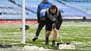Petugas membersihkan salju yang menutupi rumput jelang laga Manchester City melawan PSG pada laga semifinal Liga Champions di Stadion Etihad, Rabu (5/5/2021). (AFP/Paul Ellis)