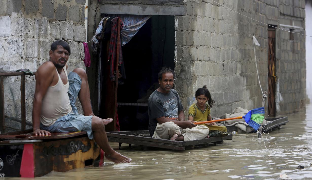 Warga duduk di luar rumah mereka di jalan banjir setelah hujan deras, di Karachi, Pakistan, Selasa (30/7/2019). Hujan deras yang melanda kota Karachi, pelabuhan selatan Pakistan, memicu banjir dan menewaskan enam orang. Pihak berwenang menutup sekolah. (AP/Photo/Fareed Khan)