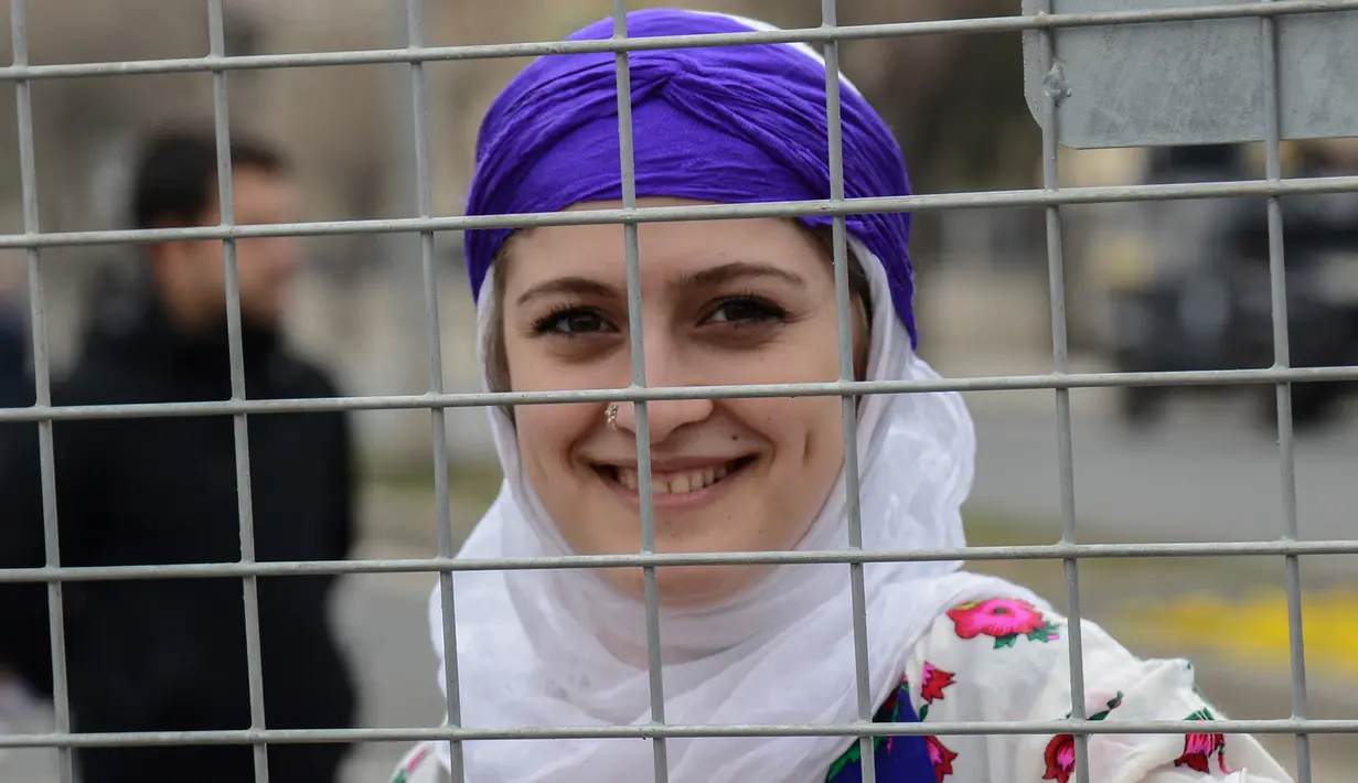 Seorang wanita berpose di belakang pagar polisi saat memperingati Women's Day atau Hari Perempuan Internasional di Diyarbakir, Turki, Kamis (8/3). (ILYAS AKENGIN/AFP)