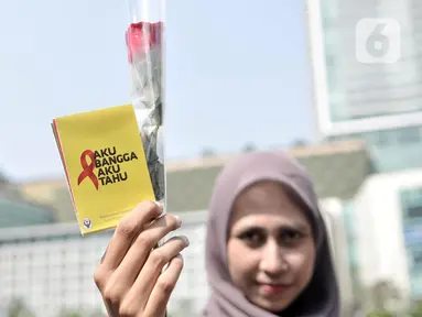 Seorang wanita menunjukkan bunga mawar dan buku panduan saat peringatan Hari AIDS Sedunia di Bundaran HI, Jakarta, Minggu (1/12/2019). Kegiatan ini bertujuan mengedukasi masyarakat tentang penyakit AIDS dan mengajak untuk peduli serta tidak menjauhkan penderita AIDS. (merdeka.com/Iqbal S. Nugroho)