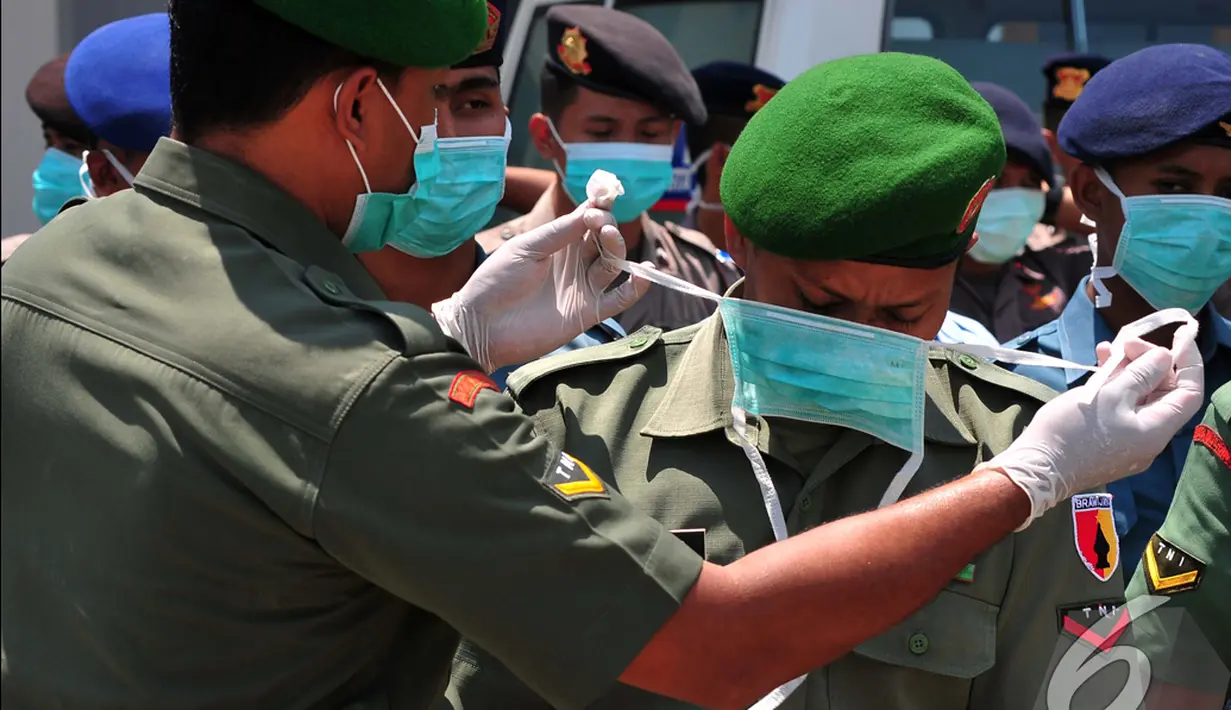 Seorang anggota dari Tim Gabungan SAR TNI membantu rekannya memakai masker saat bersiap menerima 4 jenazah penumpang AirAsia QZ8501, Surabaya, Kamis (1/1/2015). (Liputan6.com/Johan Tallo)