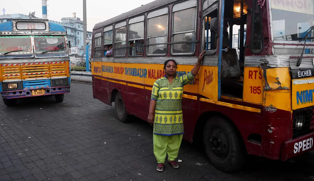 Pratima Poddar berpose di samping bus saat menunggu penumpang di Kolkata, India (8/3). Pratima Poddar 42 tahun merupakan satu-satunya sopir bus umum perempuan di Kolkata. (AFP Photo/Dibyangshu Sarkar)