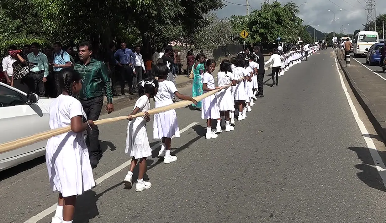 Ratusan siswa membawa saree sepanjang dua mil (3,2 Km) yang dipakai pengantin wanita saat menyusuri jalan utama di pusat kota Kandy, 22 September 2017. Kain sari itu disebut yang terpanjang yang pernah dikenakan mempelai wanita di Sri Lanka. (STR/AFP)