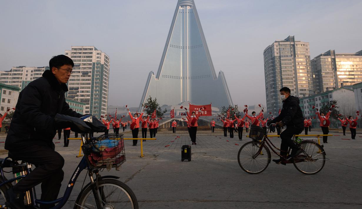 Pengendara sepeda melintasi kelompok Serikat Wanita Sosialis yang sedang melakukan propaganda di depan Hotel Ryugyong, Pyongyang, Korea Utara, Sabtu (9/3). Sebagian besar anggotanya berusia 30-50 tahun. (Ed Jones/AFP)