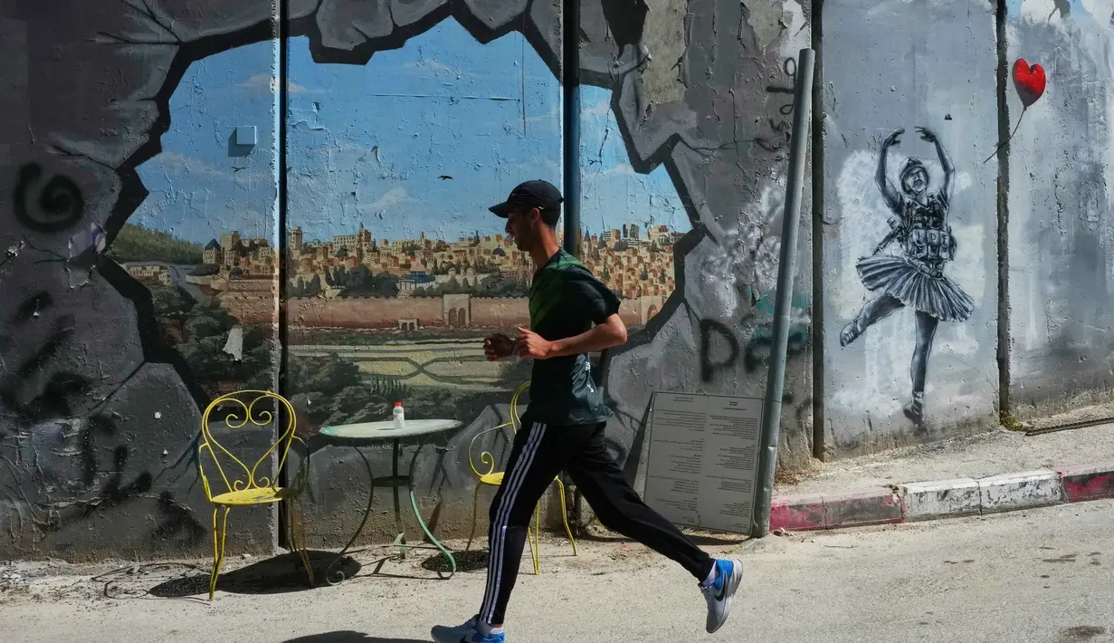 Ajang tahunan ini menekankan solidaritas dan hak untuk bergerak bagi warga Palestina. Tampak dalam foto, seorang pria berlari melewati tembok pemisah Israel saat ia berkompetisi dalam Maraton Palestina di kota Betlehem, Tepi Barat, Jumat 8 Mei 2026. (AP Photo/Mahmoud Illean)