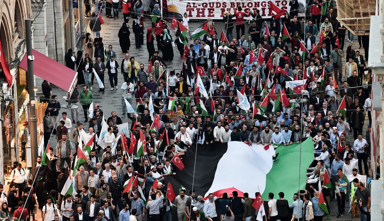 Para pengunjuk rasa membawa bendera Turki dan membentangkan bendera Palestina saat menggelar aksi menolak perpindahan kedutaan AS dari Tel Aviv ke Yerusalem di Istikilal di Istanbul, Turki (14/5). (AFP/Ozan Kose)