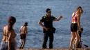 Petugas polisi meminta orang-orang untuk tidak duduk sambil berpatroli di pantai di Barcelona, Spanyol, Rabu, (20/5/2020). Barcelona mengizinkan orang untuk berjalan di pantai untuk pertama kalinya sejak dimulainya penguncian virus coronavirus lebih dari dua bulan lalu. (AP Photo/Emilio Morenatti)