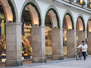 Pejalan kaki berjalan melewati etalase toko sembari menuntun sepeda di Munich, Jerman (11/12/2020). Kasus penularan dan kematian harian COVID-19 di Jerman terus meningkat dan mencapai rekor tertinggi baru pada Jumat (11/12), menurut data dari Robert Koch Institute (RKI). (Xinhua/Philippe Ruiz)