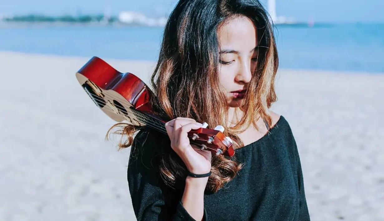 Kecintaan wanita 32 tahun ini terhadap musik membuat ia tetap membawa sebauah ukulele saat tengah berlibur. Ia juga memilih menggunakan baju bermodel off shoulder berwarna hitam dan mengurai rambutnya. (Liputan6.com/IG/@thenadiavega)
