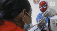 Tenaga kesehatan bertopeng superhero memperlihatkan botol vaksin covid-19 kepada orang tua anak saat vaksinasi anak usia 6-11 tahun di RSIA Tambak, Jakarta, Rabu (22/12/2021). Penggunaan topeng superhero dimaksudkan menarik minat anak-anak yang mengikuti vaksinasi. (lLiputan6.com/Herman Zakharia)