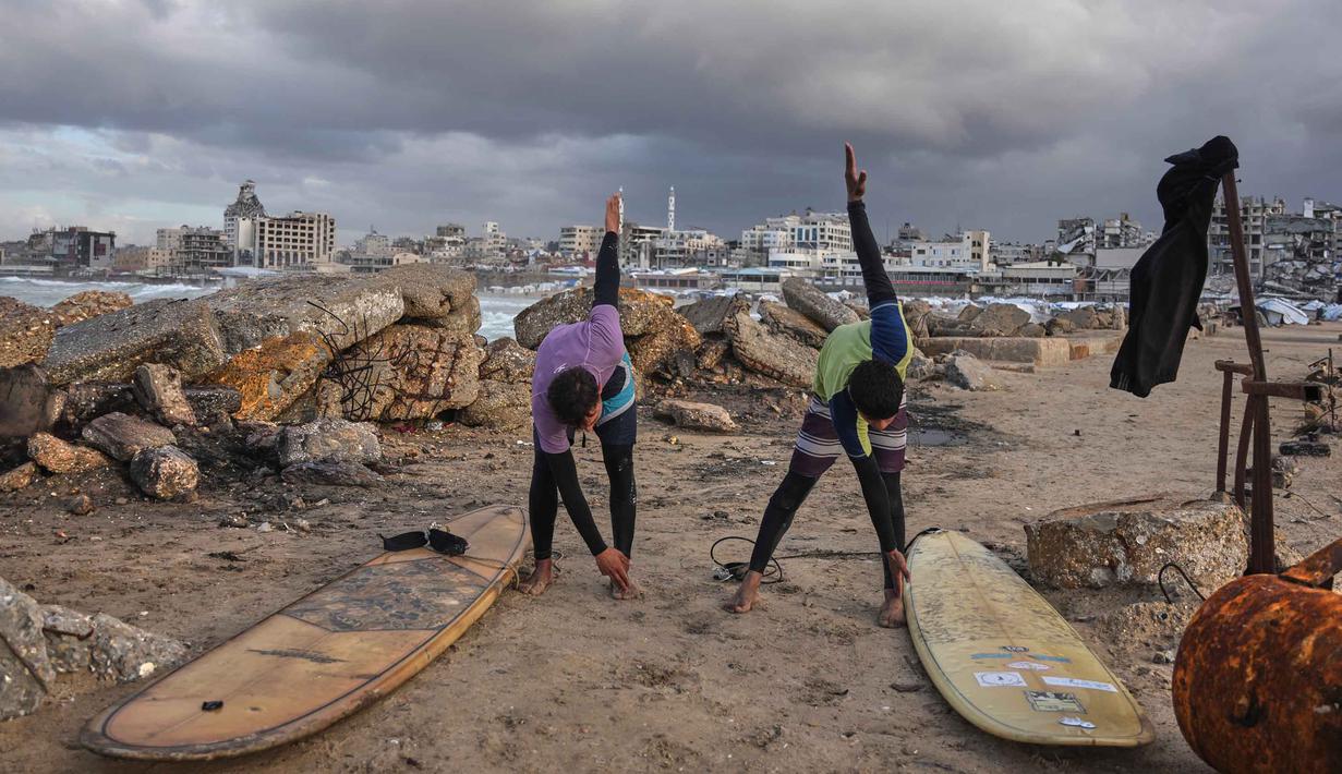 Warga Palestina, Khalil Abu Jayyab (kanan) dan Tahseen Abu Assi melakukan pemanasan sebelum berselancar di pantai Kota Gaza, Minggu, 28 Desember 2025. Pasca diberlakukannya gencatan senjata fase pertama yang didukung oleh Amerika Serikat mulai berlaku pada 10 Oktober 2025, warga Palestina mulai kembali ke Kota Gaza. (AP Photo/Jehad Alshrafi)