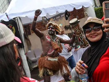 Warga berswafoto dengan suku dari Papua yang sedang menabuh gendang saat mengkampanyekan Sail Teluk Cenderawasih bertepatan dengan Hari Bebas Kendaraan Bermotor (HBKB), Kawasan Thamrin, Jakarta, Minggu (8/10/2023). (Liputan6.com/Angga Yuniar)