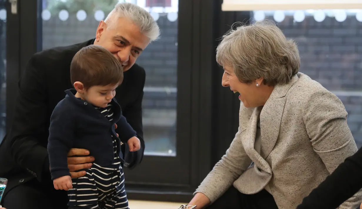 Perdana Menteri Inggris Theresa May tertawa saat bermain dengan bayi di pusat kesehatan di London, Inggris, Kamis (22/11). Sebelum menjabat sebagai PM Inggris, Theresa aktif menjadi menteri sejak tahun 2004. (Andrew Matthews/Pool via AP)