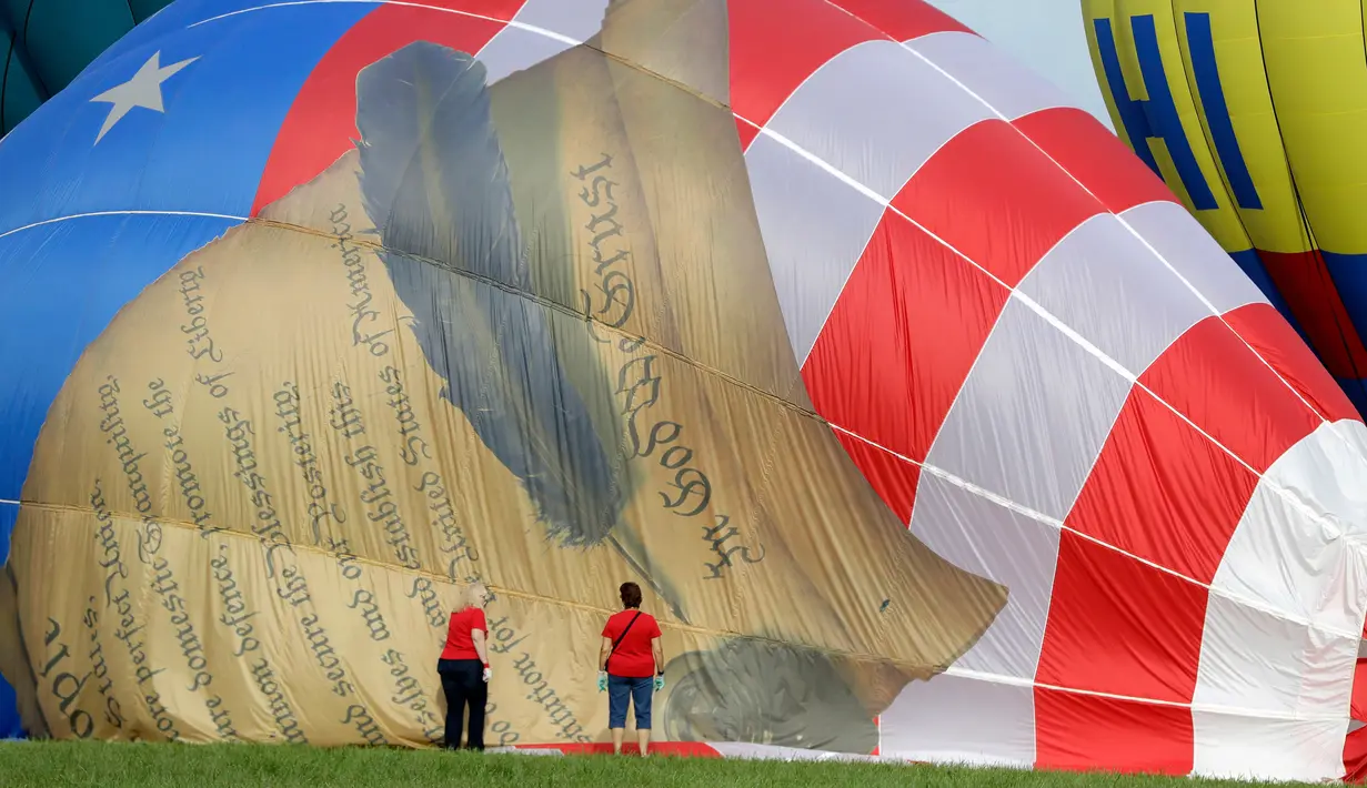 Dua orang wanita membantu mengempiskan balon dengan lukisan Konstitusi Amerika Serikat saat Festival Balon QuickChek New Jersey di Kota Readington, New Jersey (28/7). (AP Photo/Julio Cortez)