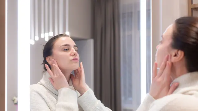 Seorang perempuan sedang bercermin sambil menyentuh rahangnya (Foto Dok: Freepik/kroshka__nastya)