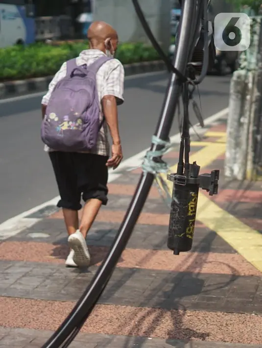 Pejalan kaki melintasi samping instalasi kabel yang semrawut di Jalan Kyai Maja, Kebayoran Baru, Jakarta Selatan, Rabu (11/11/2020). Kurangnya penataan menjadi penyebab instalasi kabel di Ibu Kota kian semrawut sehingga mengganggu kenyamanan serta keselamatan warga. (Liputan6.com/Immanuel Antonius)
