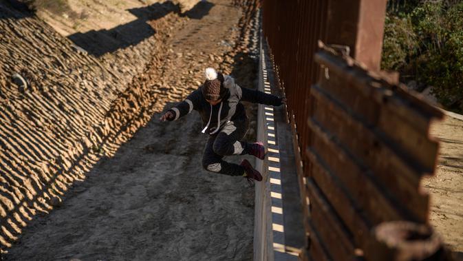 Nelly, imigran Meksiko dari Oaxaca, melompati pagar perbatasan untuk masuk ke sisi AS ke San Diego, California, (28/12). Aksi imigran ilegal ini dilakukan demi bisa menembus perbatasan AS yang semakin ketat. (AP Photo/Daniel Ochoa de Olza)