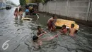 Sejumlah anak bermain di genangan air banjir di Kawasan Muara Angke, Jakarta, Rabu (11/1). Banjir ini juga telah merendam ratusan rumah, toko, dan tempat pengeringan ikan asin. (Liputan6.com/Gempur M. Surya)