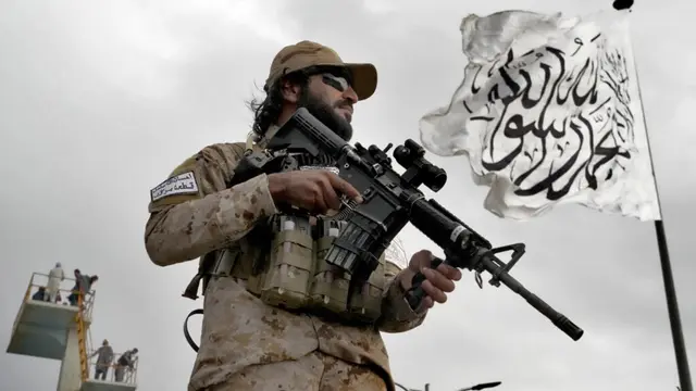 Seorang penjaga pasukan khusus Taliban berdiri di depan bendera Taliban di Kabul, Afghanistan, 18 April 2022. (Ebrahim Noroozi, AP)