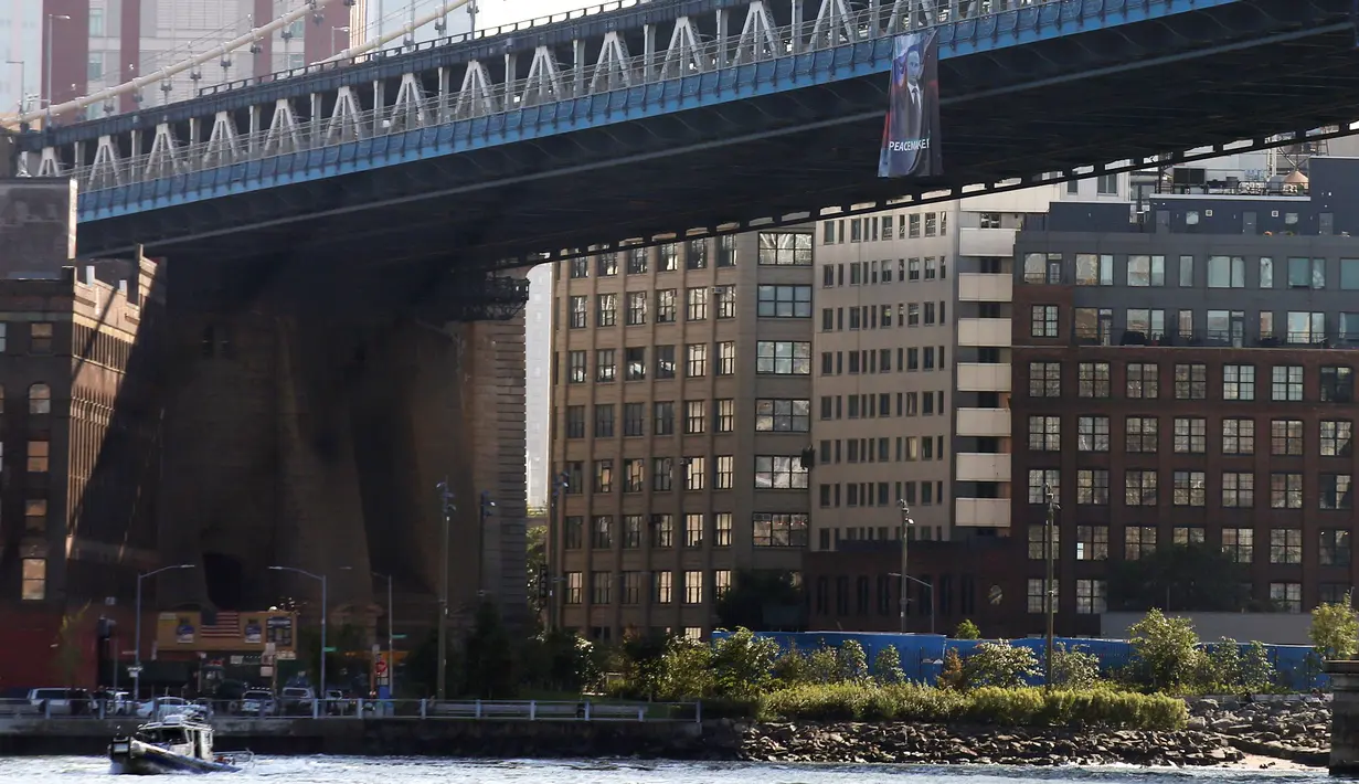 Sebuah kapal melintas di bawah banner bergambar Presiden Rusia Vladimir Putin yang tergantung di Jembatan Manhattan, New York, Kamis (6/10). Terdapat tulisan ‘PEACEMAKER’ (pendamai) yang dicetak tebal pada banner tersebut. (REUTERS/Brendan McDermid)