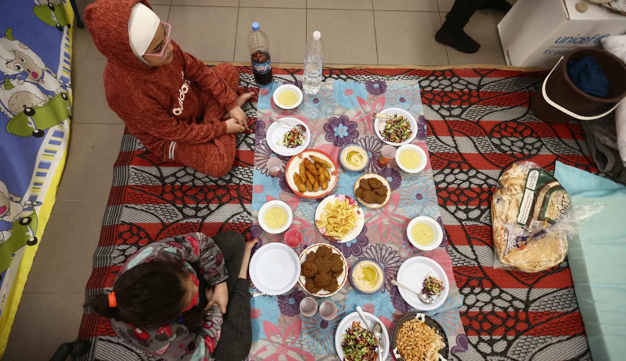 117.228 orang pengungsi tinggal di 538 tempat pengungsian resmi di seluruh Lebanon, sementara yang lain mendaftar secara daring di luar tempat penampungan melalui platform moza-relief.com. Tampak dalam foto, anak-anak pengungsi yang tinggal bersama keluarga mereka di ruang kelas sekolah, setelah melarikan diri dari serangan udara Israel di pinggiran selatan Beirut, Lebanon, duduk untuk berbuka puasa bersama, pada 7 Maret 2026. (Ibrahim AMRO/AFP)