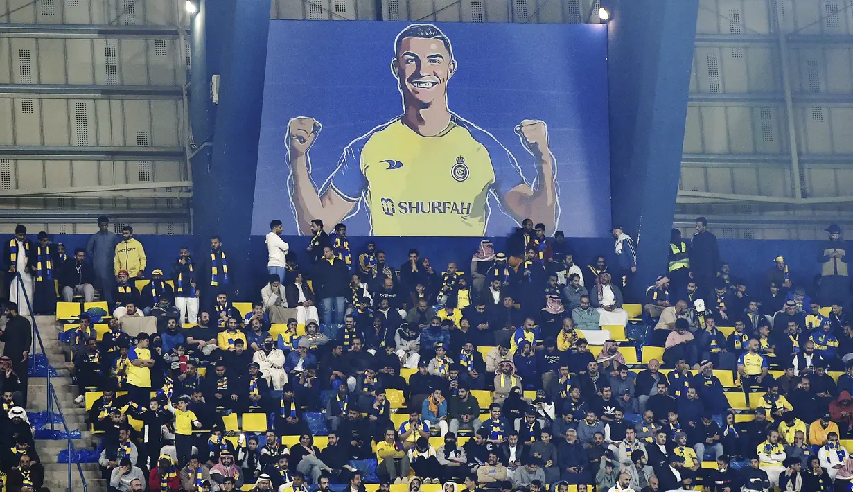 <p>Penggemar Al Nassr duduk di bawah papan reklame raksasa yang memperlihatkan Cristiano Ronaldo selama pertandingan Liga Pro Saudi antara Al Nassr dan Al Ettifaq di Stadion Mrsool Park di Riyadh, Arab Saudi, Minggu (22/1/2023). Meski Ronaldo menjadi kapten tim gagal mencetak gol dalam debutnya. (AP Photo)</p>