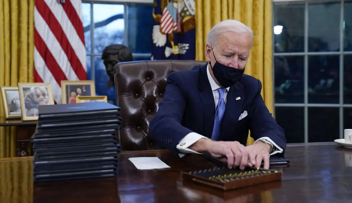 Presiden Joe Biden meraih pena untuk menandatangani perintah eksekutif pertamanya di Ruang Oval, Gedung Putih di Washington, Rabu (20/1/2021). Pada hari pertamanya menjabat, Presiden Amerika Serikat Joe Biden menandatangani sejumlah tindakan eksekutif di Gedung Putih. (AP Photo/Evan Vucci)